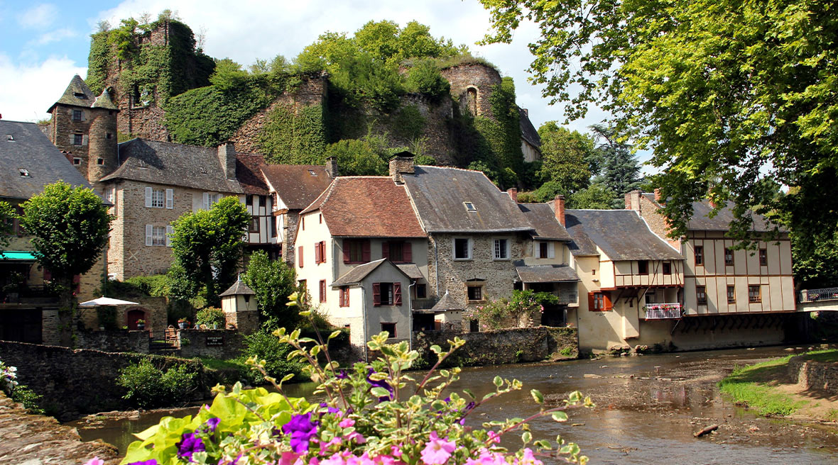 View from a bridge of a beautiful French village with pink and purple flowers and green trees nearby